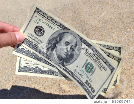 A girl takes out from the sand money notes of three hundred dollars. 61639744