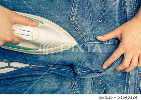 Image on top of man ironing blue jeans on ironing board 61640324