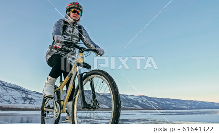 Woman is riding bicycle on the ice. Tires on bike are covered wi 61641322