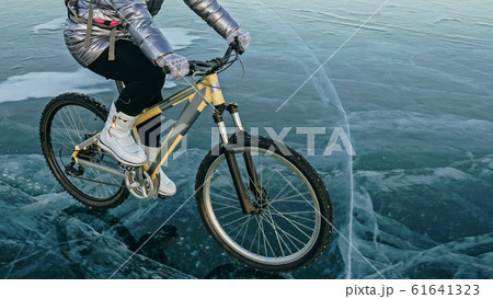 Woman is riding bicycle on the ice. Tires on bike are covered wi 61641323
