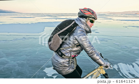 Woman is riding bicycle on the ice. Tires on bike are covered wi 61641324