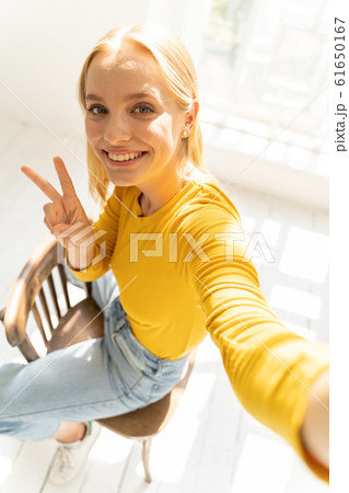 Smiling charming lady in yellow sweater sitting on chair against light background Smiling charming lady in yellow sweater sitting on chair against light background 61650167