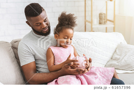 Young afro father showing little daughter piggy bank 61657396