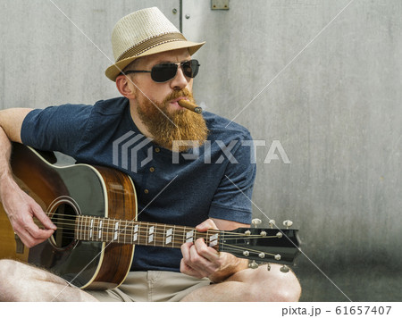 Man with fedora and cigar playing acoustic guitar 61657407
