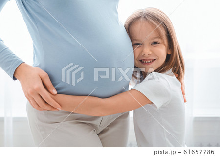 Excited little girl embracing her pregnant mother tummy 61657786