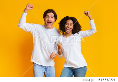 Overjoyed interracial couple celebrating success with raised fists over yellow background Overjoyed interracial couple celebrating success with raised fists over yellow background 61658354