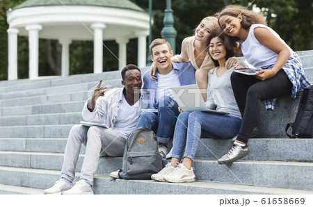 Happy students smiling at camera while doing homework outdoors Happy students smiling at camera while doing homework outdoors 61658669