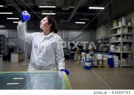 Female lab assistant with flask in hands with blue liquid Female lab assistant with flask in hands with blue liquid 61660793