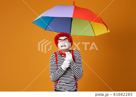 Dissatisfied mime man with multi-colored umbrella isolated on blank orange background 61662265