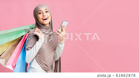 Happy islamic woman in hijab holding smartphone and paper shopping bags 61662878