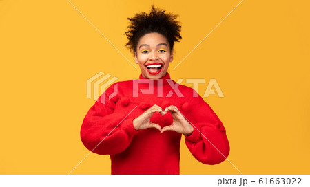Smiling black girl showing heart gesture with fingers 61663022