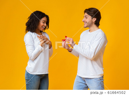 Romantic guy proposing to his surprised girlfriend, giving ring 61664502