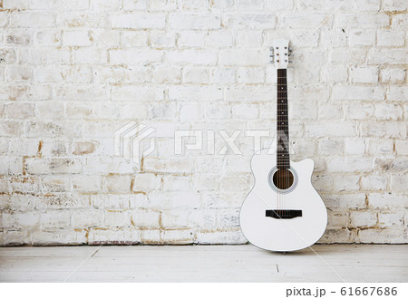 Acoustic white guitar leaning against a white wall 61667686