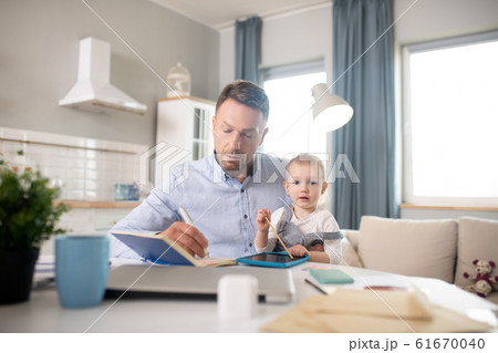 Bearded man in a blue shirt holding his kid and looking concentrated Bearded man in a blue shirt holding his kid and looking concentrated 61670040