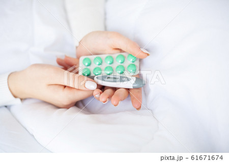 Cold and flu. Woman hold termometr and blister pills in hand, lying on the bed 61671674
