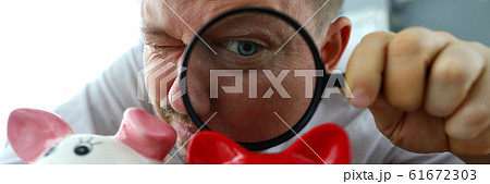 Man examining tree funny piggybanks with magnifying glass 61672303