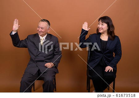 Happy mature Asian businessman and mature Asian businesswoman waving hands together 61673518