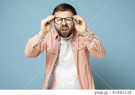 A poorly seeing Caucasian man took off glasses, squinted, and looked through the transparent lenses. 61682136