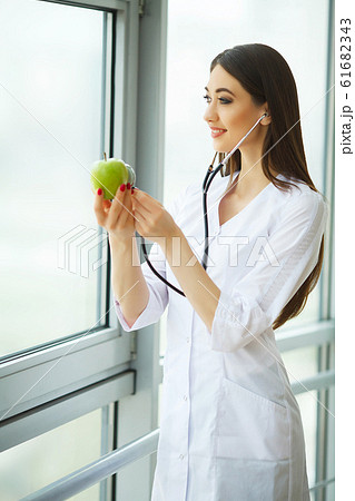 Health. Healthy Diet. Doctor Dietitian Holding in Hands Fresh Green Apple and Smiles. Beautiful and Young Doctor. High Resolution 61682343