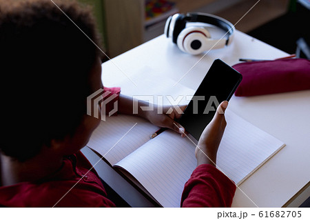 Schoolboy sitting at a desk using a smartphone in an elementary school classroom Schoolboy sitting at a desk using a smartphone in an elementary school classroom 61682705