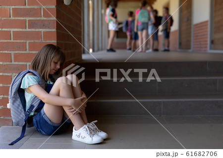 Schoolgirl  sitting on the ground alone in the schoolyard at elementary school 61682706