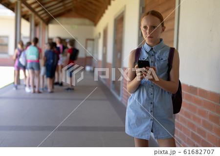 schoolgirl standing in the schoolyard at elementary school using a smartphone schoolgirl standing in the schoolyard at elementary school using a smartphone 61682707