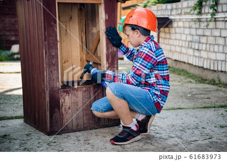Boy burns the wall of a wooden house. son helps parents with painting the garden house 61683973