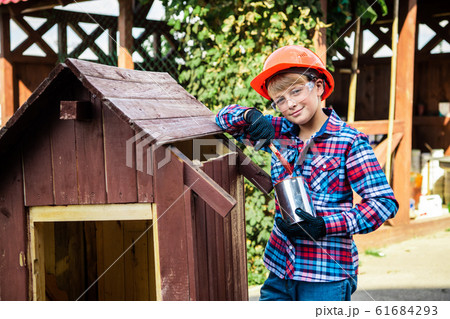 Boy paints the wall of a wooden house. son helps parents with painting the garden house Boy paints the wall of a wooden house. son helps parents with painting the garden house 61684293