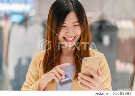 Asian woman using credit card with mobile phone for online shopping in department store over the clothes shop store background, technology money wallet and online payment concept, credit card mockup Asian woman using credit card with mobile phone for online shopping in department store over the clothes shop store background, technology money wallet and online payment concept, credit card mockup 61685988