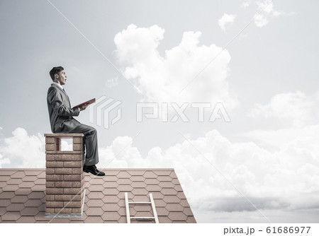 Student guy in suit on brick house roof reading book 61686977
