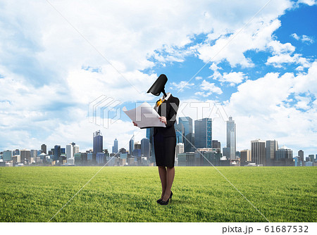Camera headed woman standing on green grass against modern cityscape 61687532