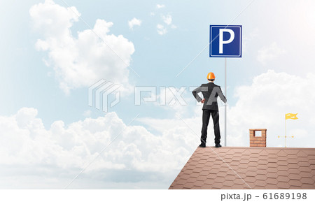 Young businessman with parking sign standing on brick roof. Mixed media 61689198
