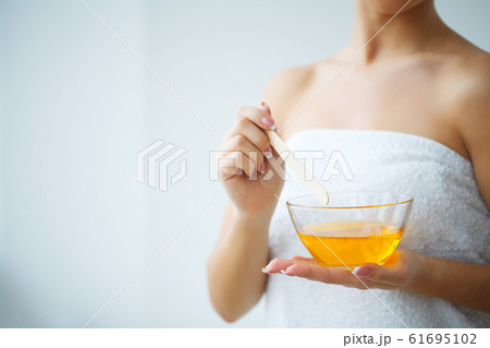 Women hold orange paraffin wax bowl. Woman in beauty salon 61695102