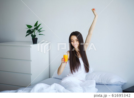 Cheerful woman drinking an orange juice sitting on her bed Cheerful woman drinking an orange juice sitting on her bed 61695342
