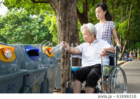 Asian little child girl or granddaughter and senior grandmother hand putting plastic water bottle in recycling bin,elderly tourist in wheelchair,hand throwing garbage in a trash bin,environmental prot 61696316