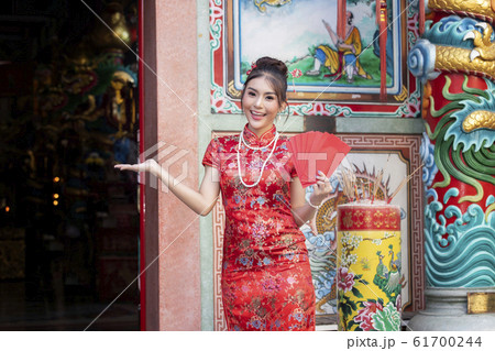 Chinese woman in a red cheongsam (qipao) dress holding red envelopes (hong bao) at shrine. 61700244