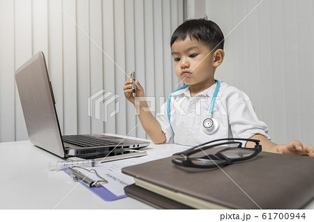 little boy in medic uniform holding a pen on desk. little boy in medic uniform holding a pen on desk. 61700944