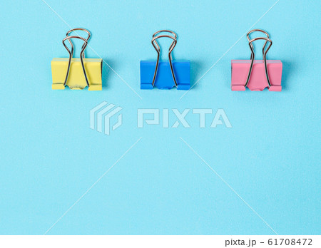 Colorful binder clips on blue paper background. Colorful binder clips on blue paper background. 61708472