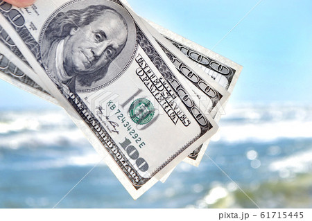 Girl holding money bill of 300 dollars on background of sea ocean Girl holding money bill of 300 dollars on background of sea ocean 61715445