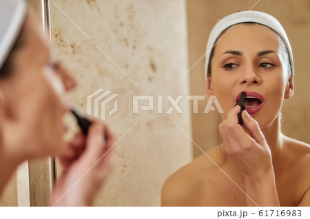 Beautiful woman applies makeup in front of bathroom mirror 61716983