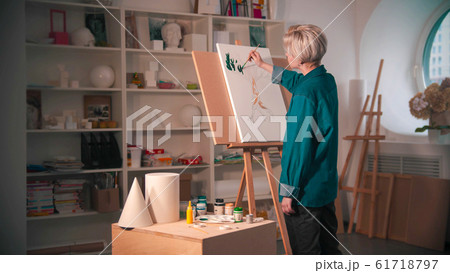 A young woman artist with short hair painting upper branches of tree in green color in the art studio A young woman artist with short hair painting upper branches of tree in green color in the art studio 61718797