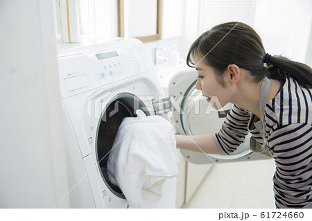ドラム式洗濯機に洗濯物を入れる若い女性の写真素材