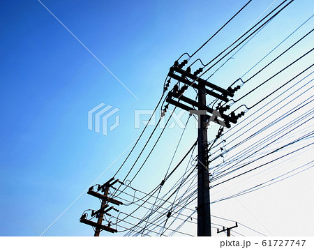 Silhouettes of high tension and low tension power lines on poles. On the bright blue morning sky background with copy space. Selective focus Silhouettes of high tension and low tension power lines on poles. On the bright blue morning sky background with copy space. Selective focus 61727747