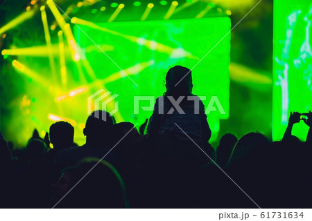 Silhouette of a big crowd at concert against a brightly lit stage. Night time rock concert with people having fun lifting hands up in the air and cheering the musicians Silhouette of a big crowd at concert against a brightly lit stage. Night time rock concert with people having fun lifting hands up in the air and cheering the musicians 61731634