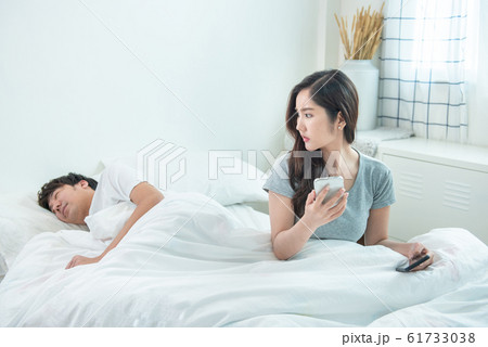wife spying the phone of her husband while man sleeping in bed at home. 61733038