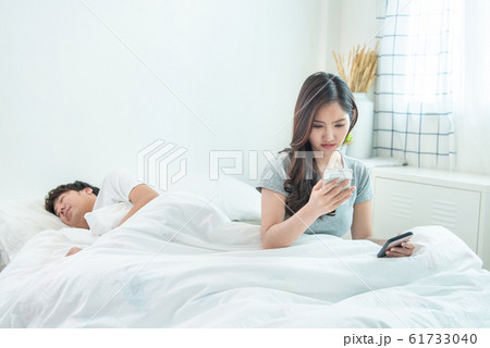 wife spying the phone of her husband while man sleeping in bed at home. 61733040