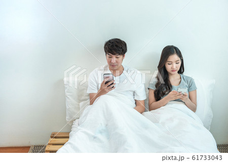 Young asian couple in bed using phone lying backs on wall,relationship problem with technology. 61733043