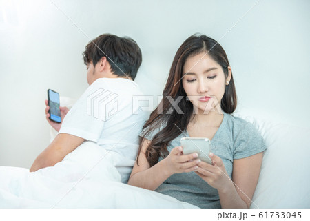 Asian couple in bed using phone lying backs to each other relationship problem with technology. 61733045