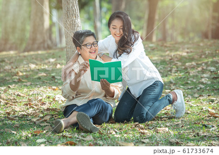 Elder asian mother and daughter read book in wood on green grass lawn,concept of happy family life 61733674