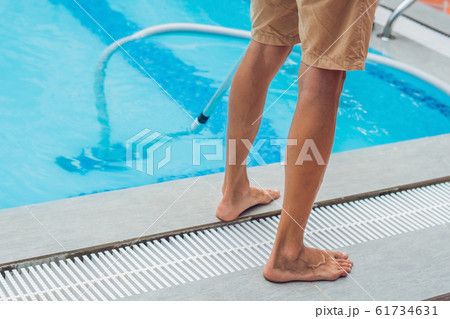 Cleaner of the swimming pool . Man in a blue shirt with cleaning equipment for swimming pools, sunny 61734631